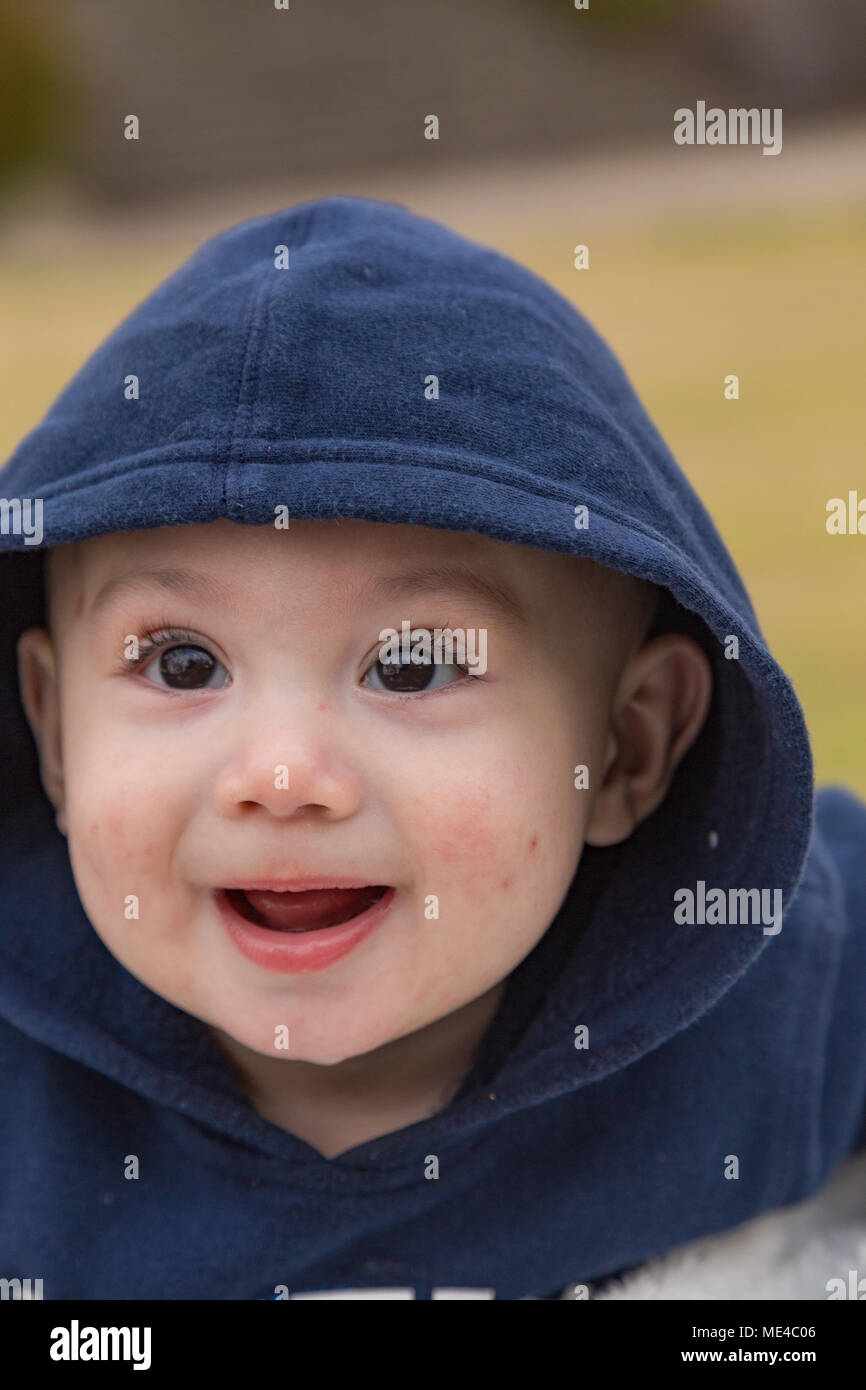 Baby boy in hoodie smiling with big eyes at the park. Stock Photo