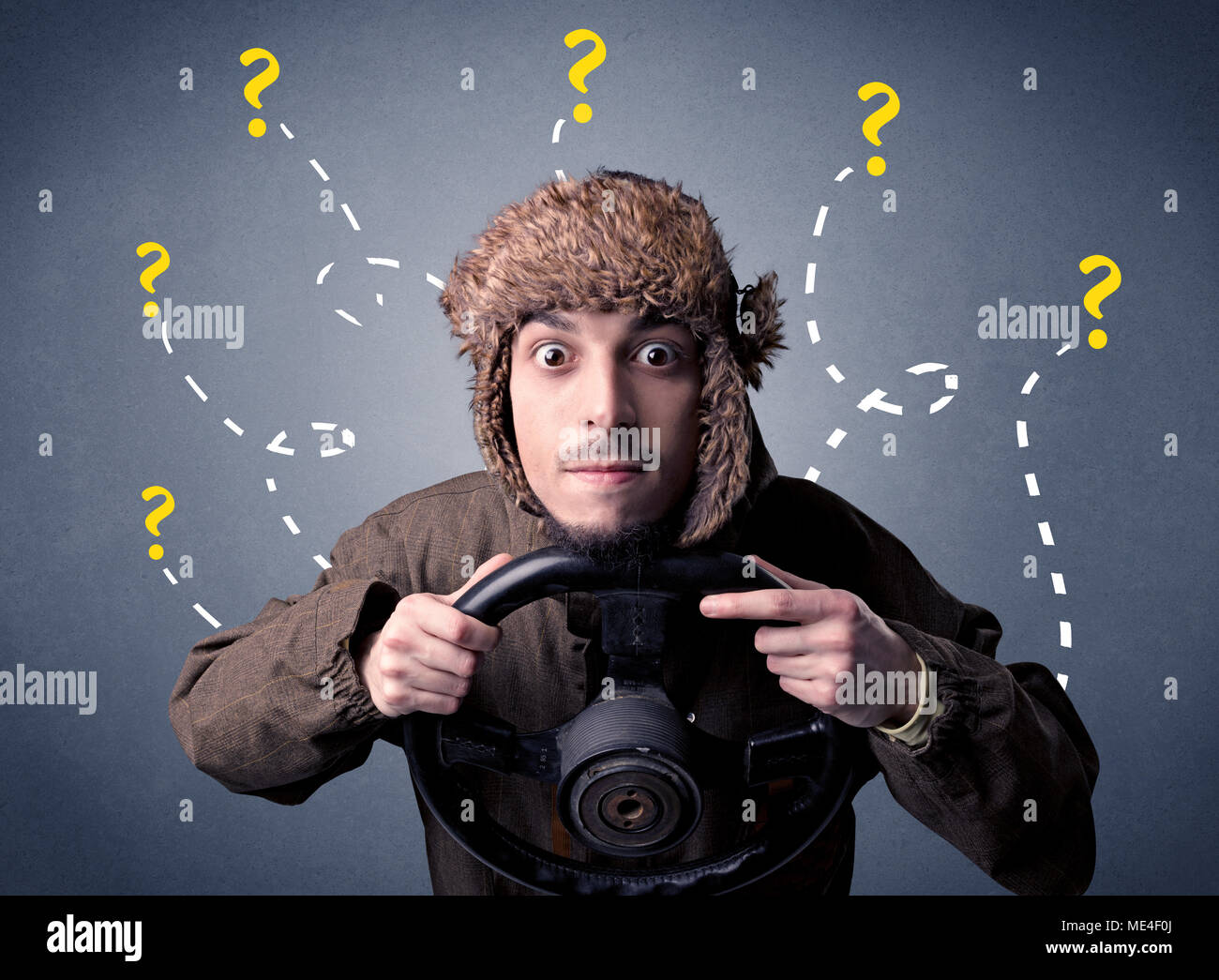 Young man holding black steering wheel with question marks around him