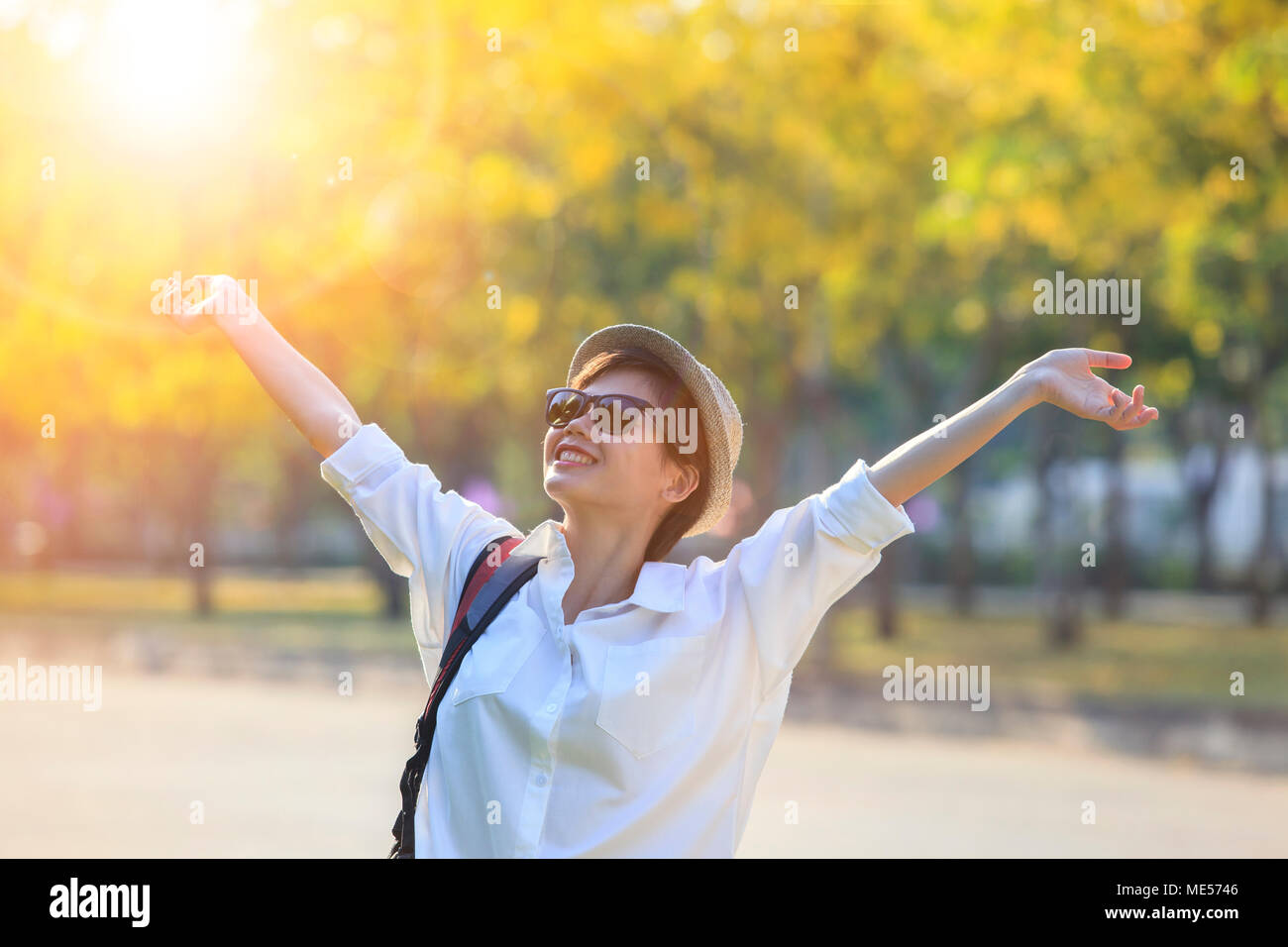 young asian woman wearing white shirt and sun glasses rising hand with freedom feeling in pulbic park Stock Photo