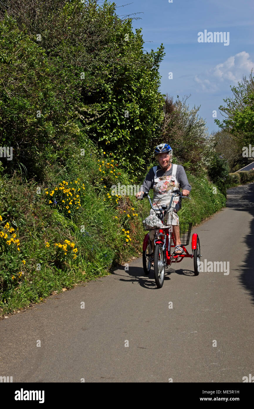 Elderly lady riding red battery assisted tricycle on country lane