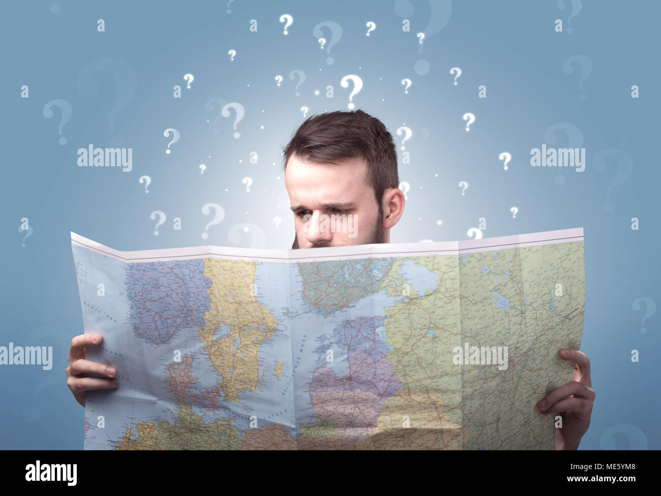Handsome young man holding a map with white question marks above his ...