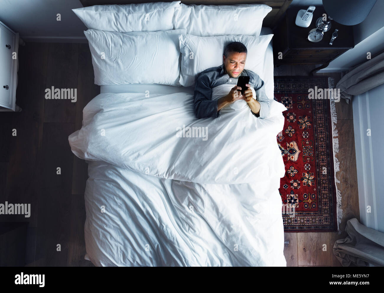 Man on bed using his cellphone Stock Photo