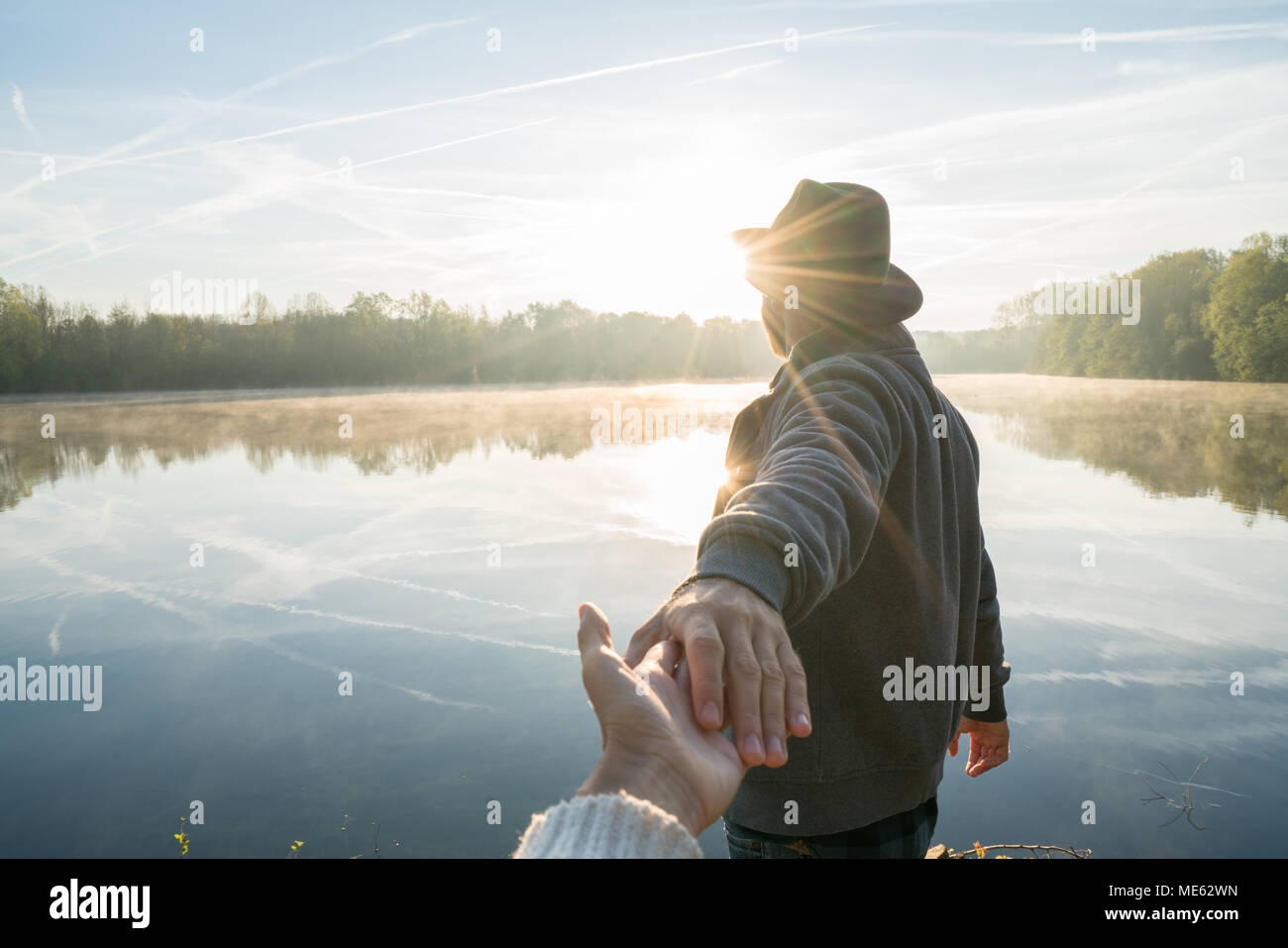 Follow me to concept, young man leading girlfriend to the lake at sunrise, people travel journey concept sharing. Personal perspective Stock Photo