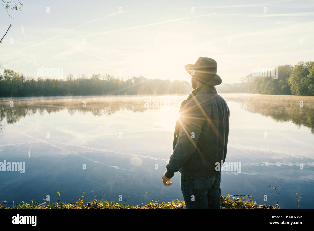Young man contemplating nature by the lake at sunrise, springtime, France, Europe. People travel relaxation in nature concept. Toned image Stock Photo