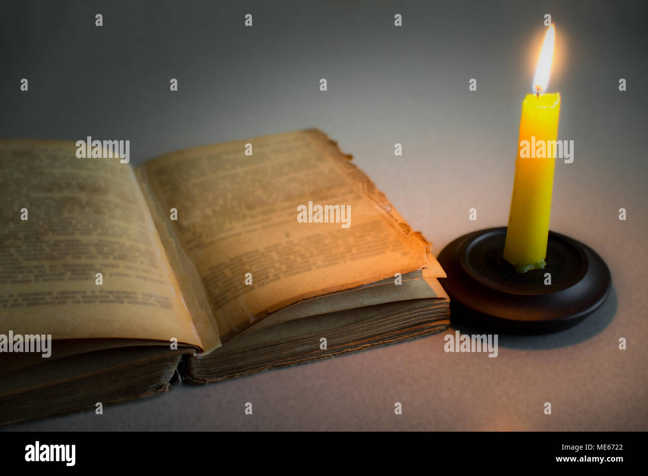 Old shabby open book and burning candle Stock Photo