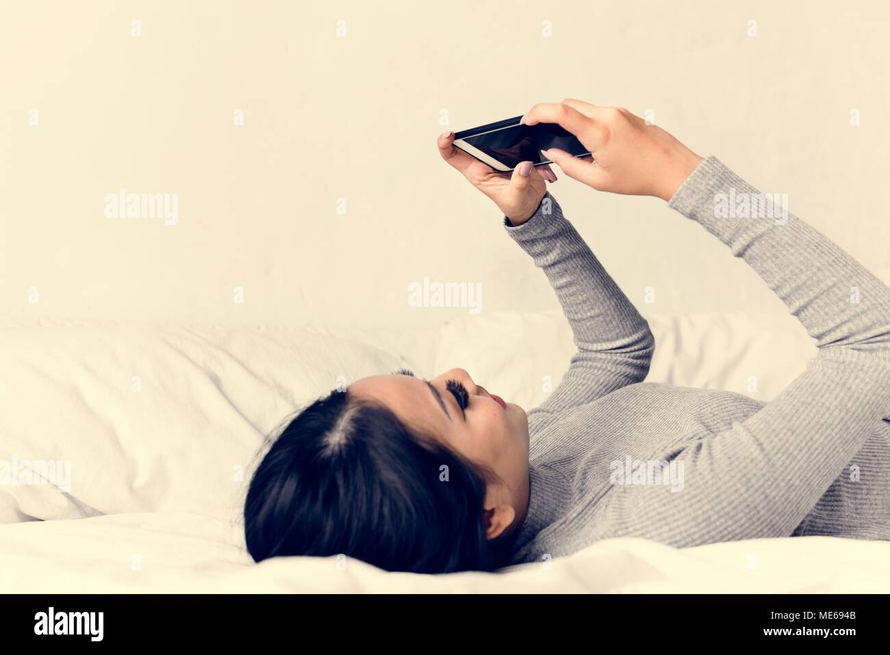 Asian woman lying on bed using mobile phone Stock Photo - Alamy