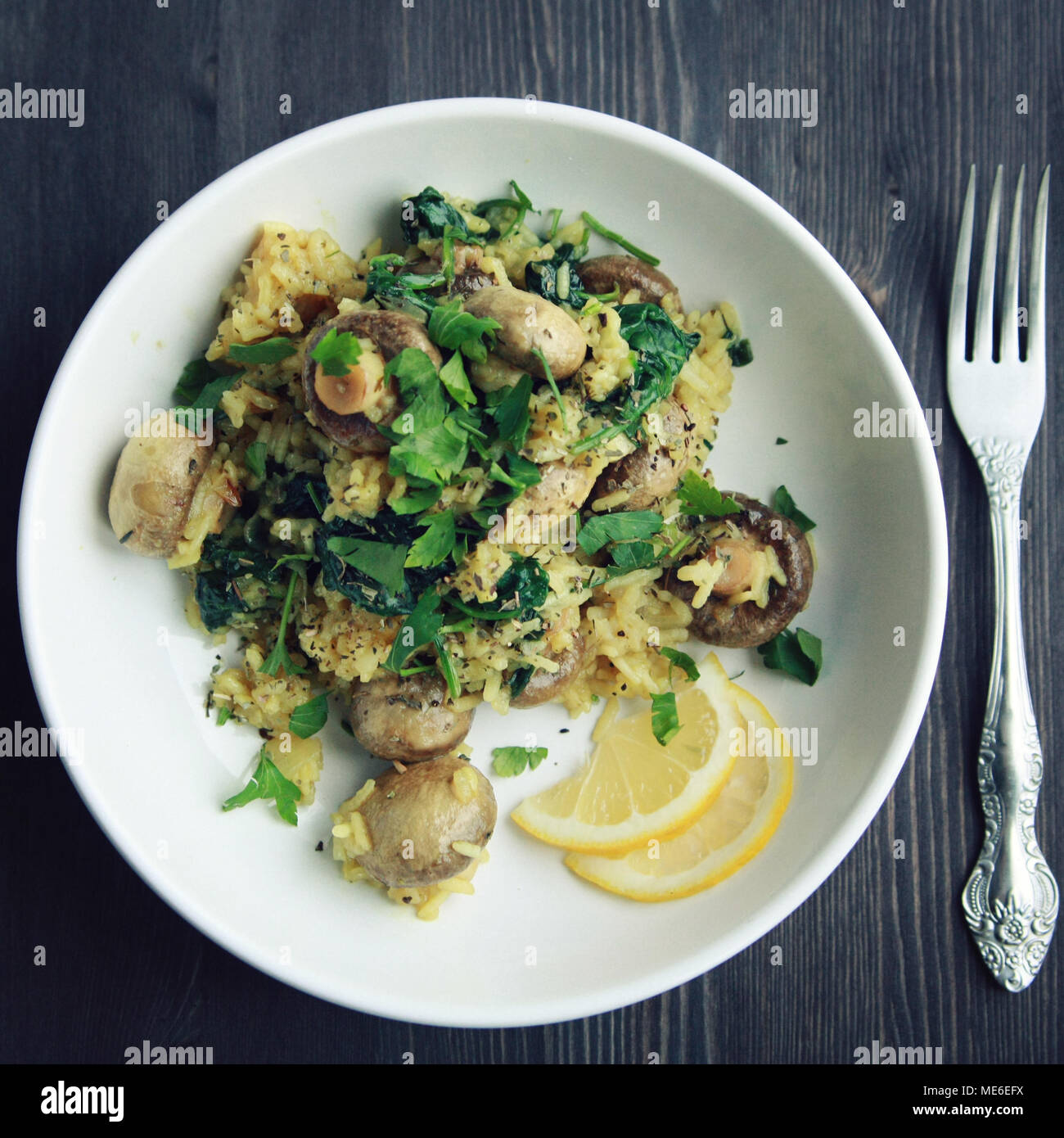 Vegetarian turmeric rice in the white bowl. Vegan dish. European cuisine. Yellow rice with mushrooms and spinach. Meatless. Toned photo. Top view. Stock Photo
