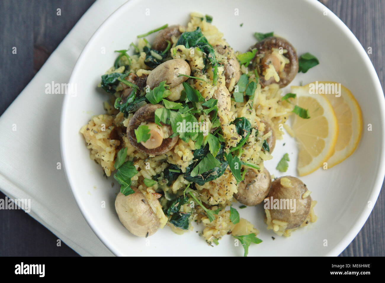 Yellow rice with mushrooms and spinach. Vegan dish. European cuisine. Vegetarian turmeric rice in the white bowl. Meatless. Top view. Stock Photo
