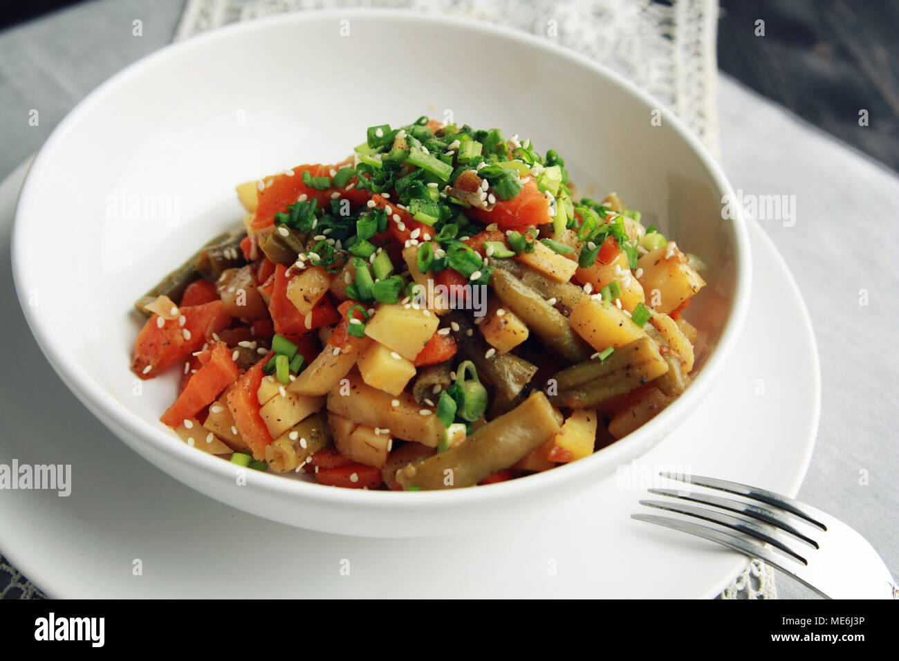 Vegetable stew with potato, carrot and green beans topped with sesame seeds. European cuisine. Healthy vegan lunch on the round white plate. European  Stock Photo