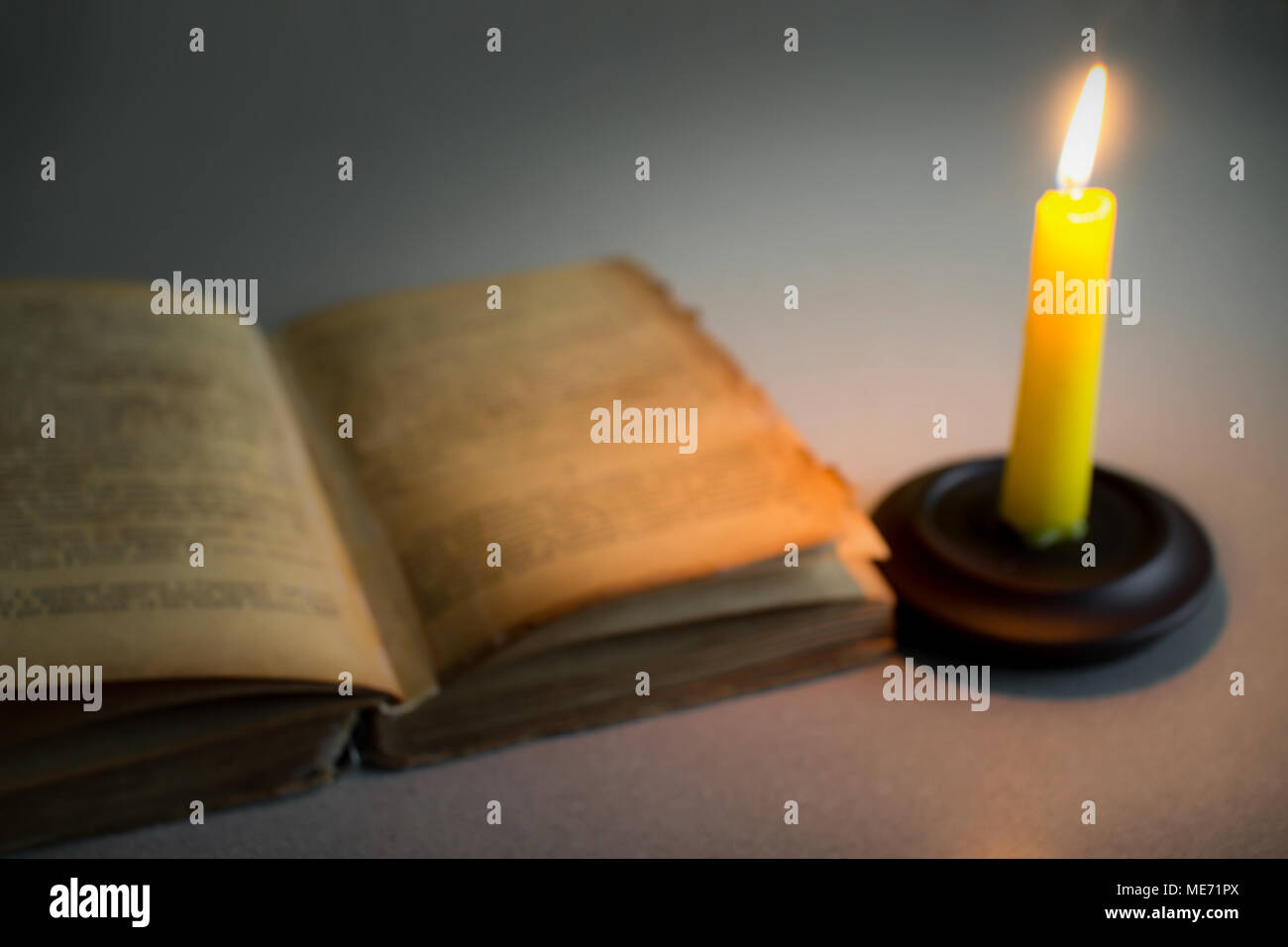 Old shabby open book and burning candle Stock Photo