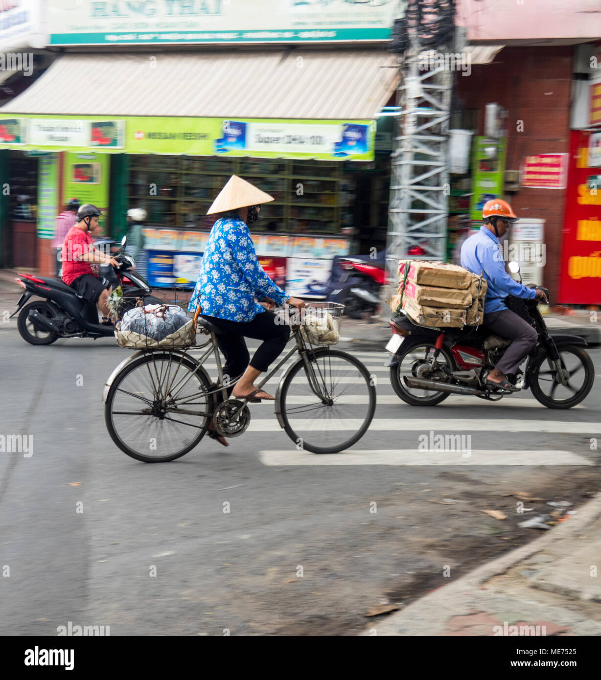 A female cyclist wearing a conical hat riding her bicycle alongside motorcycles in Ho Chi Minh City, Vietnam. Stock Photo