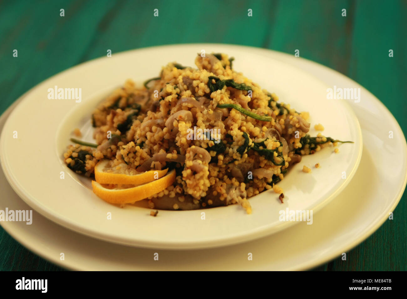 Millet with mushrooms and spinach. Vegan dish. Vegetarian couscous on the round white plate. Stock Photo