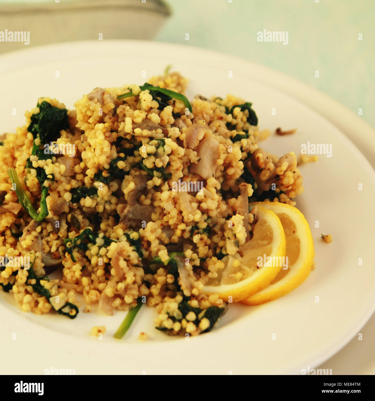 Millet with mushrooms and spinach. Jewish cuisine. Vegetarian couscous on the round white plate. Close up. Toned photo. Stock Photo