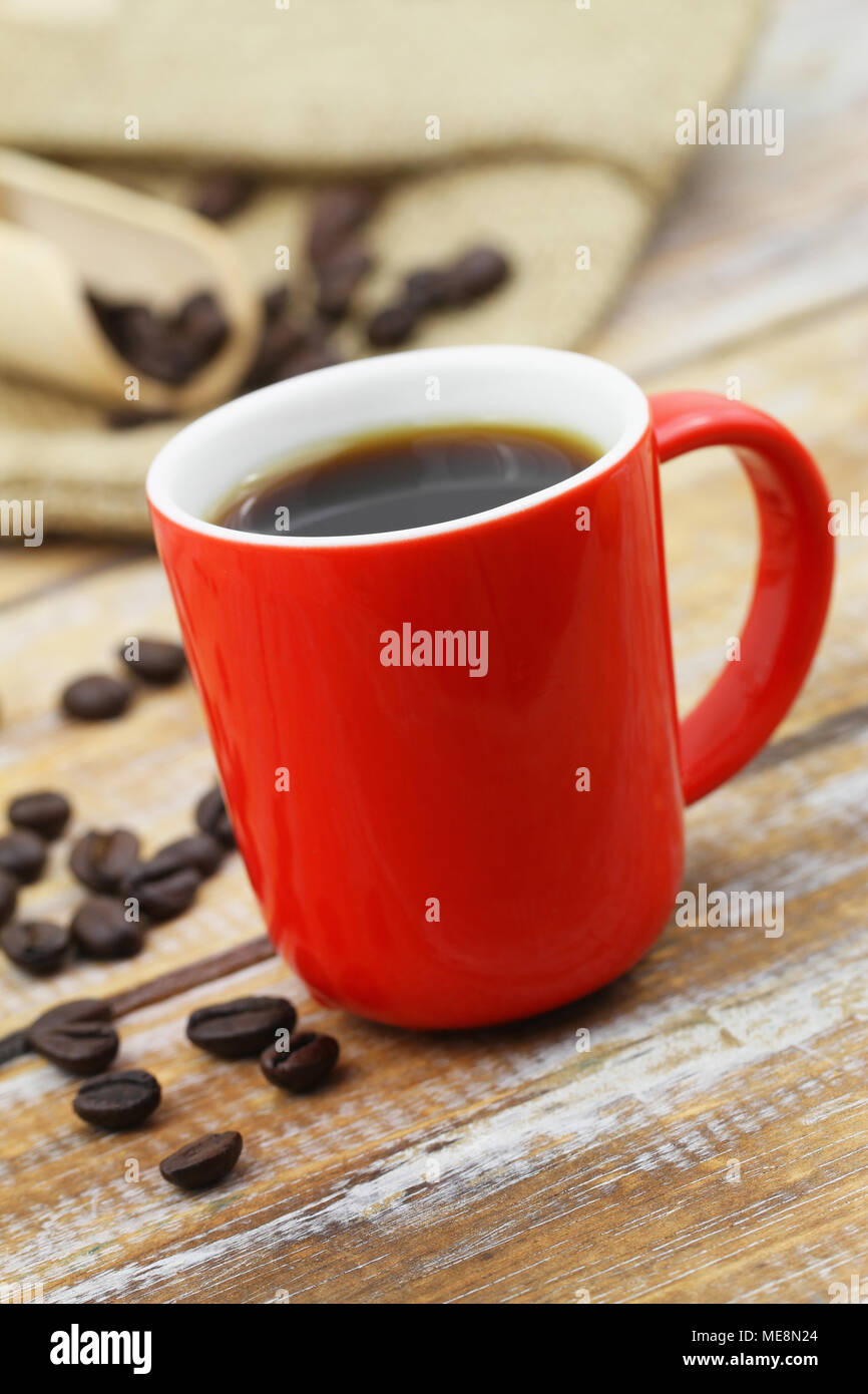 Black coffee in red mug on rustic wooden surface and scattered roasted coffee beans Stock Photo