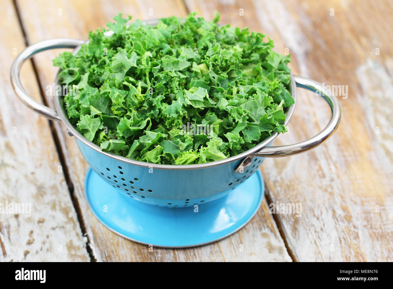 Raw kale leaves in blue colander on rustic wooden surface Stock Photo