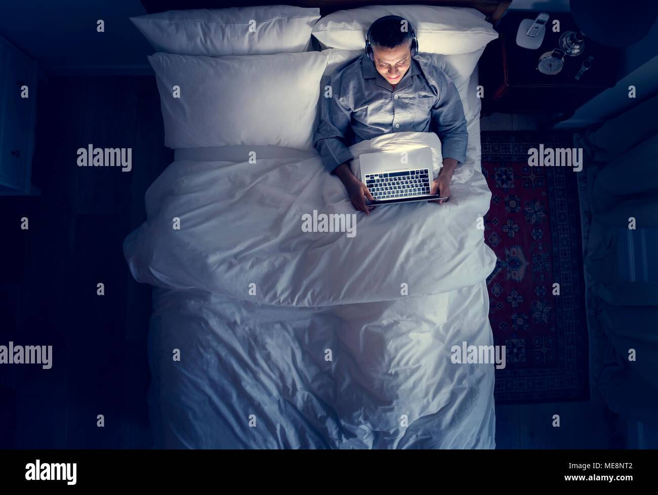 Man on bed using his laptop and a headphone Stock Photo