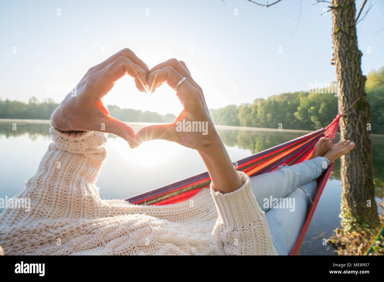 Close up on female's hands making a heart shape finger frame on lake forest landscape. Unrecognisable person. Travel love environment concept Stock Photo