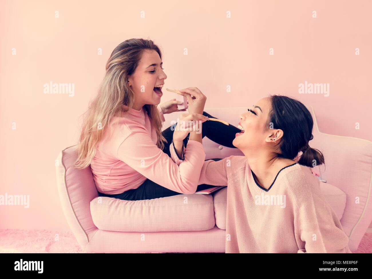 Women sitting feeding fries each other with pink background Stock Photo