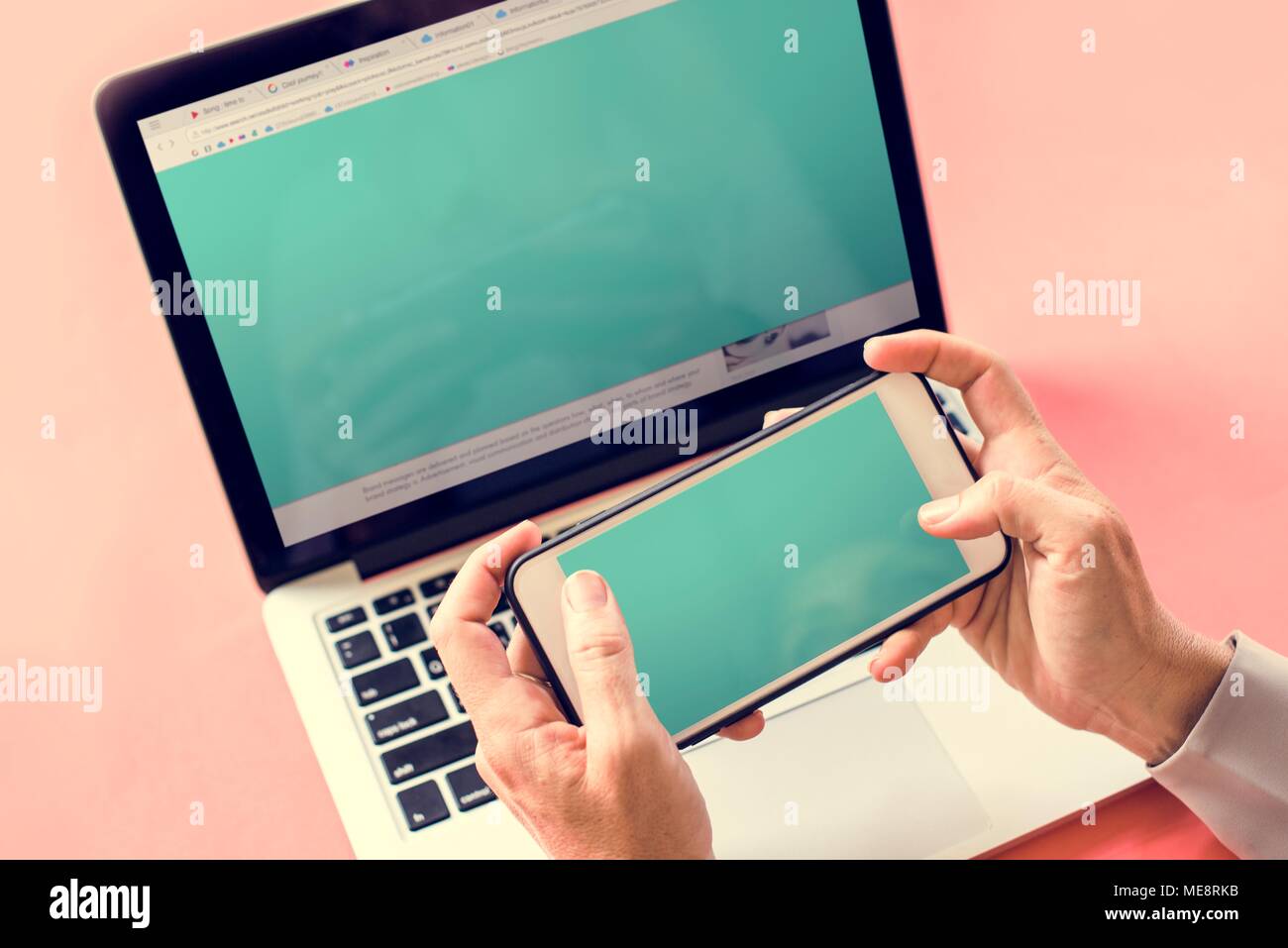 Hands holding smartphone and laptop in background Stock Photo