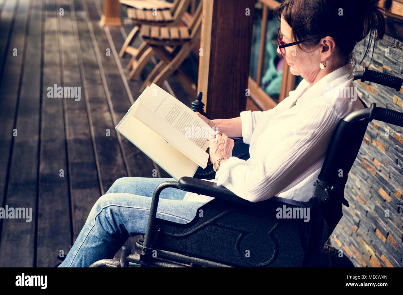 A woman sitting on a wheelchair and reading Stock Photo