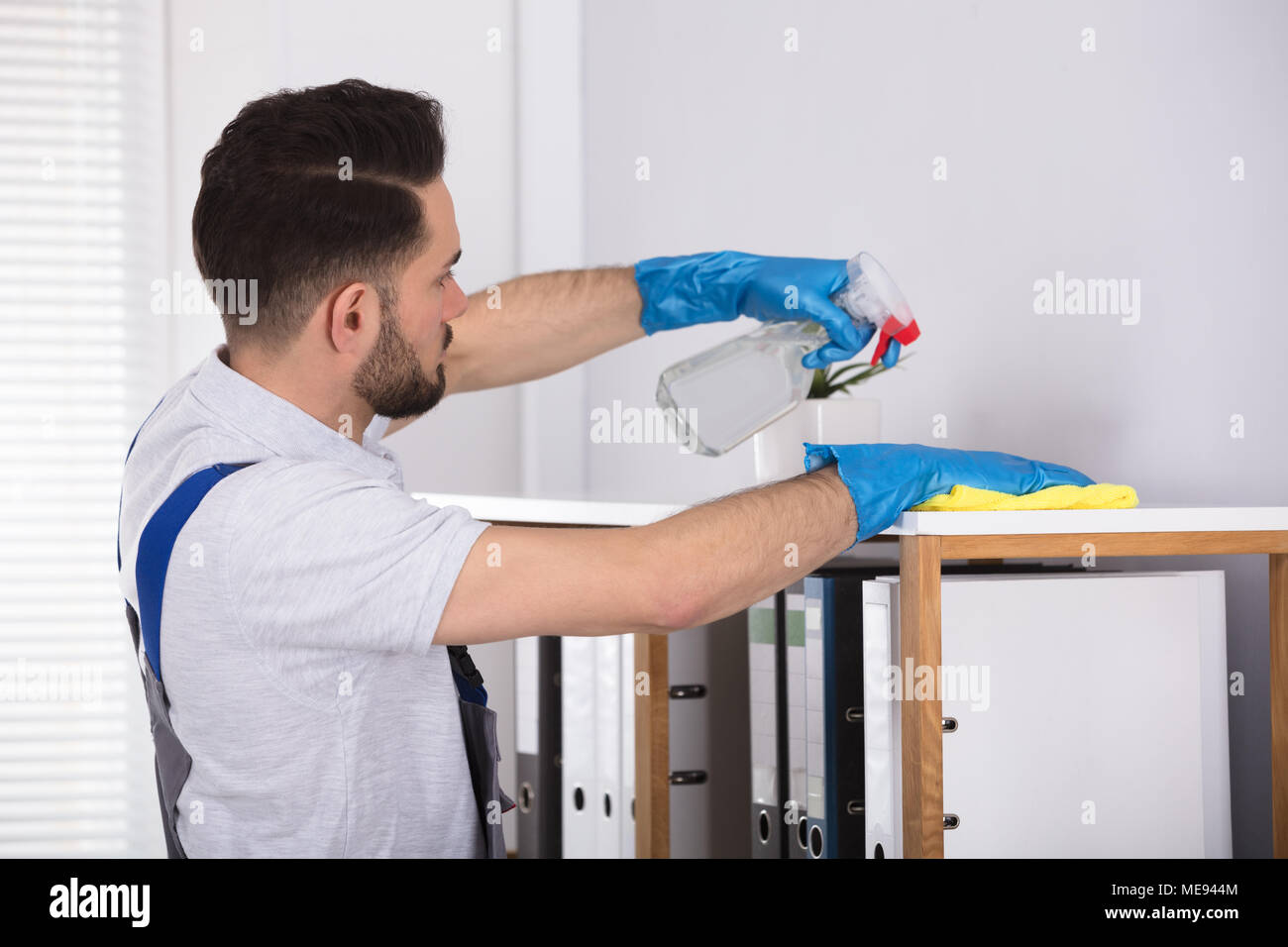 Close-up Of A Young Male Cleaner Cleaning Shelf At Workplace Stock Photo