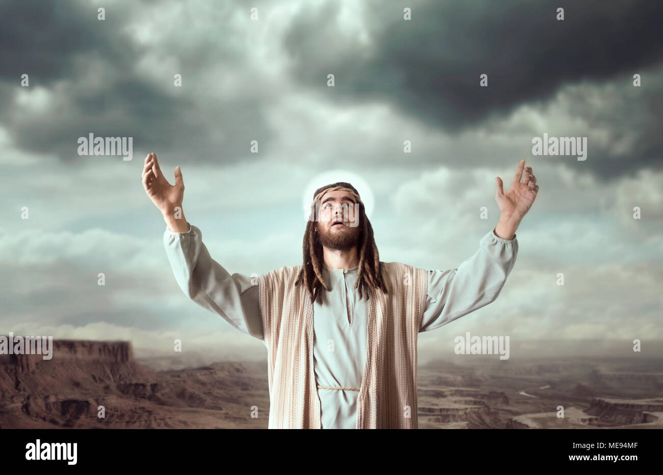 Jesus Christ in white robe praying with his hands up against cloudy sky. Strong faith in God, christianity Stock Photo