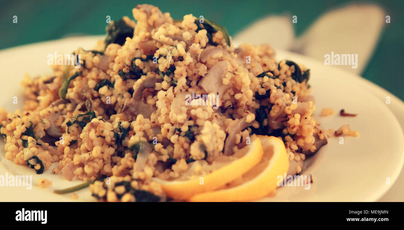 Millet with mushrooms and spinach. Jewish cuisine. Vegetarian couscous on the round white plate. Close up. Wide photo. Stock Photo