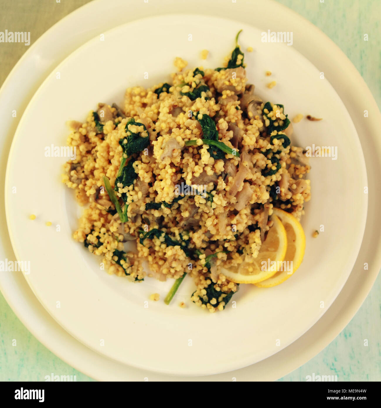 Millet with mushrooms and spinach. Vegan dish. Vegetarian couscous on the round white plate. Top view. Toned photo. Stock Photo