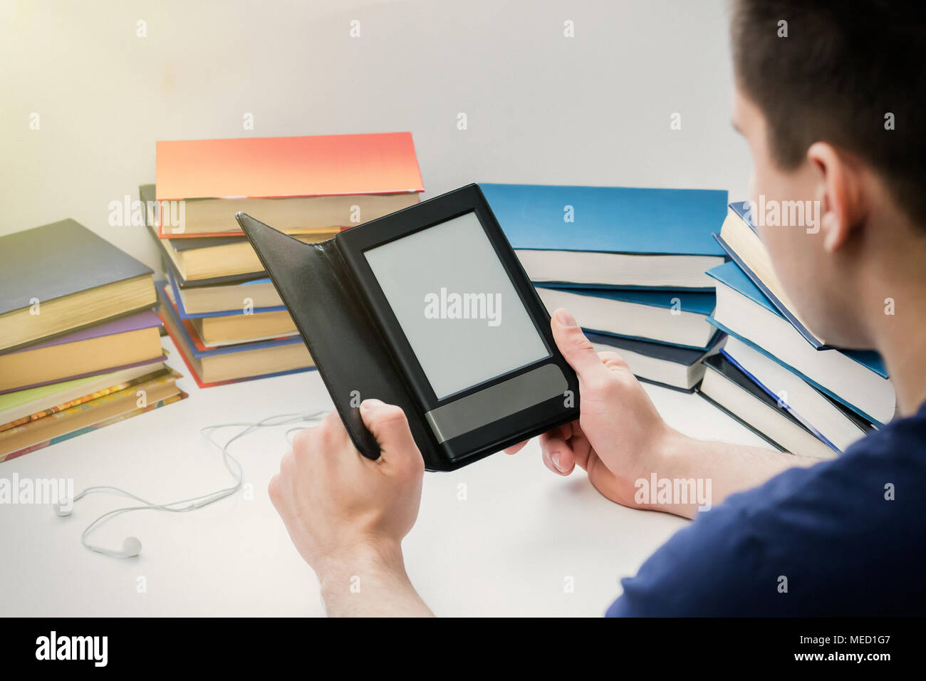 A young man is reading an e-book on the background of old paper books. The student is educated in the library. Stock Photo