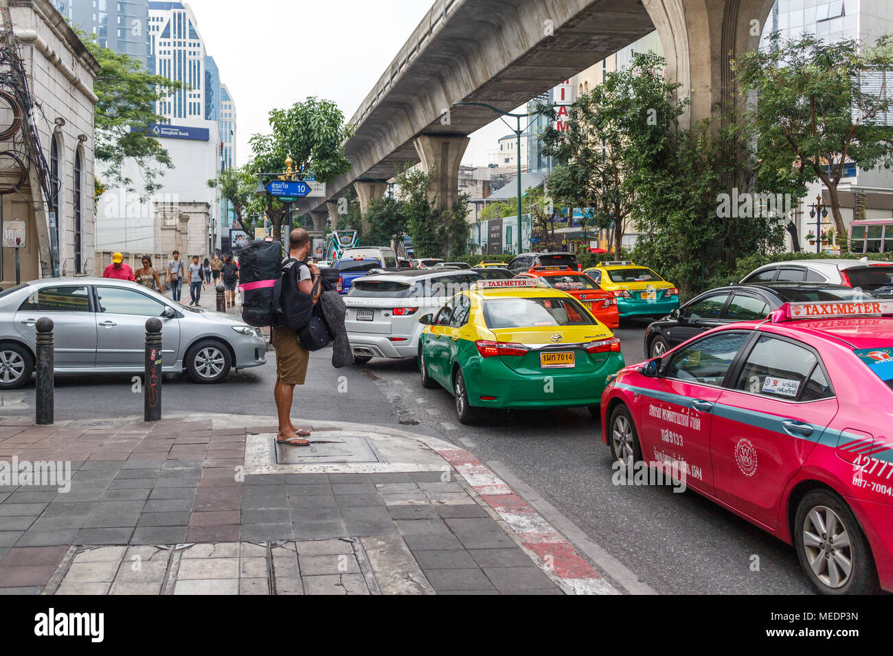 A backpacker waits for an empty taxi in heavy traffic on Sukhumvit Road, Bangkok, Thailand Stock Photo