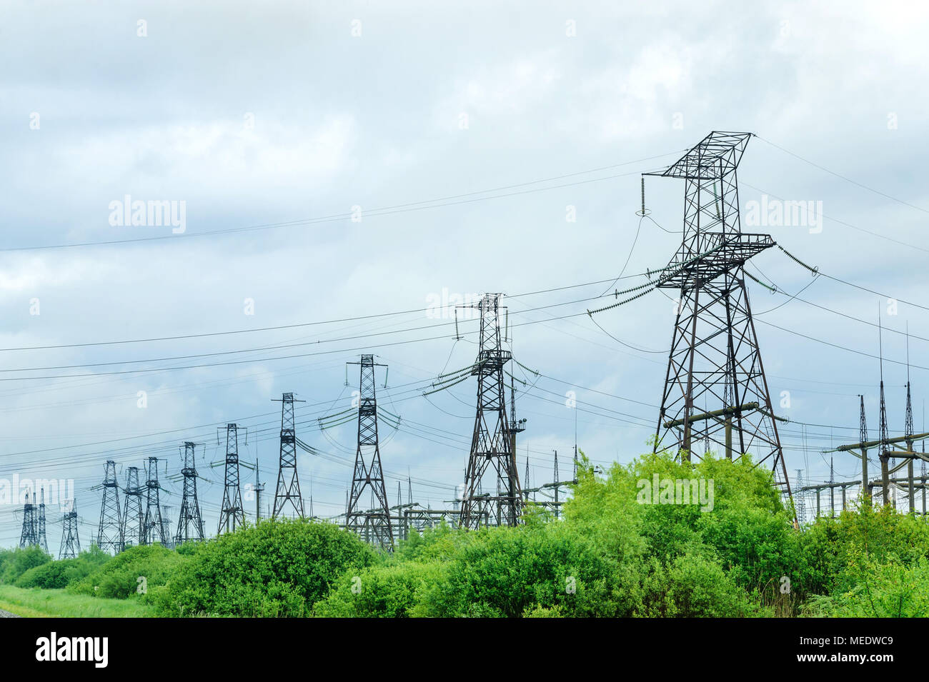 High voltage towers behind trees on background cloudy sky Stock Photo ...
