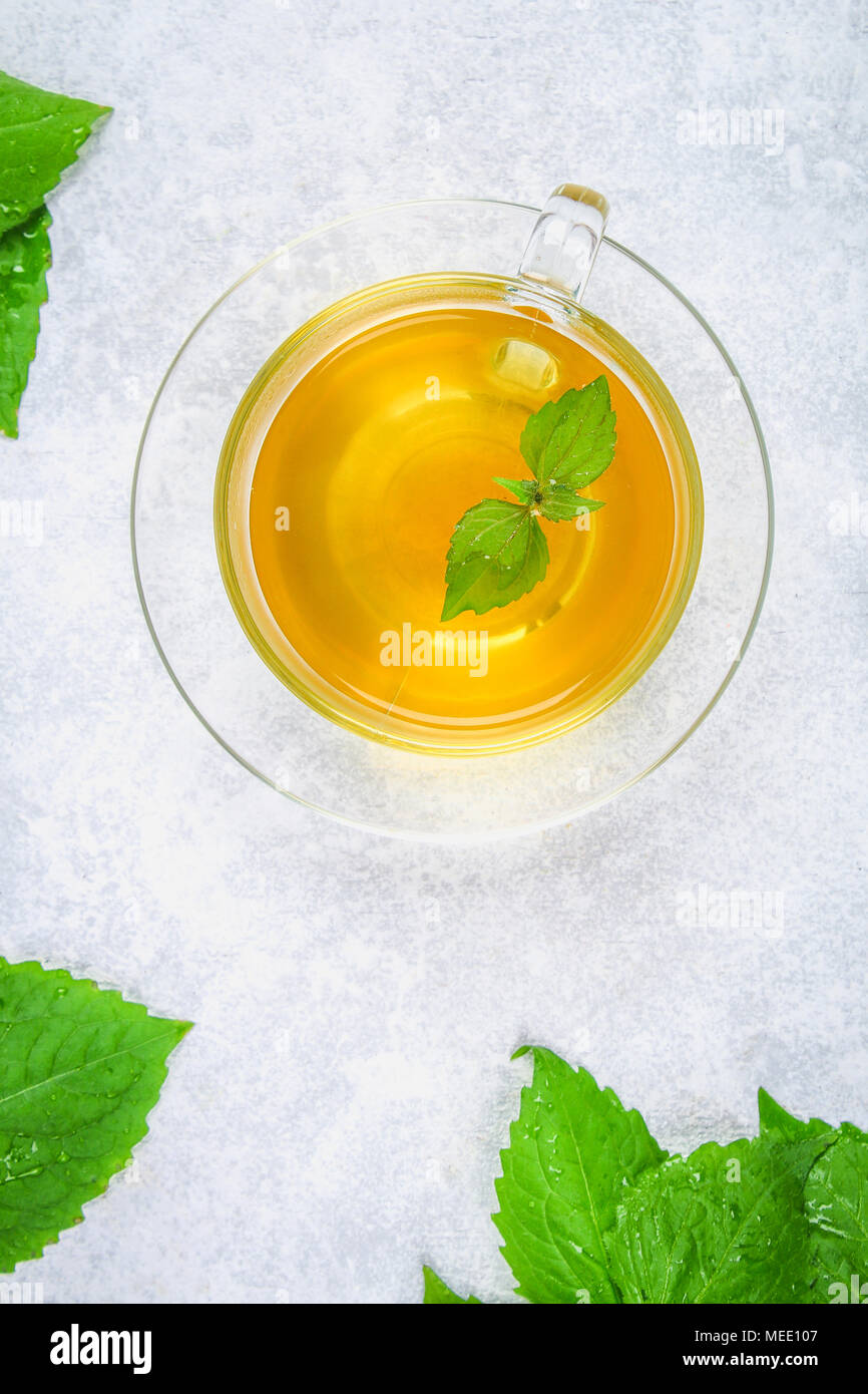 Leaves of fresh green nettle and a clear glass cup of herbal nettle tea on a gray concrete table Stock Photo