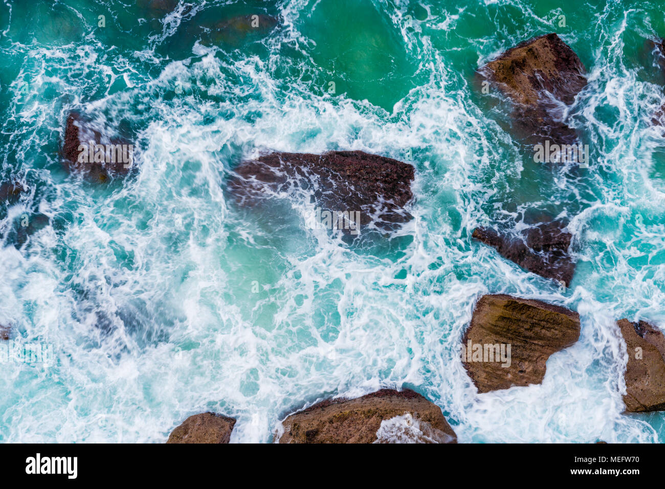 Top aerial view of blue waves crashing on rocky Australian coastline. Summer seascape with birds eye view shot over ocean waves and cliffs. Stock Photo