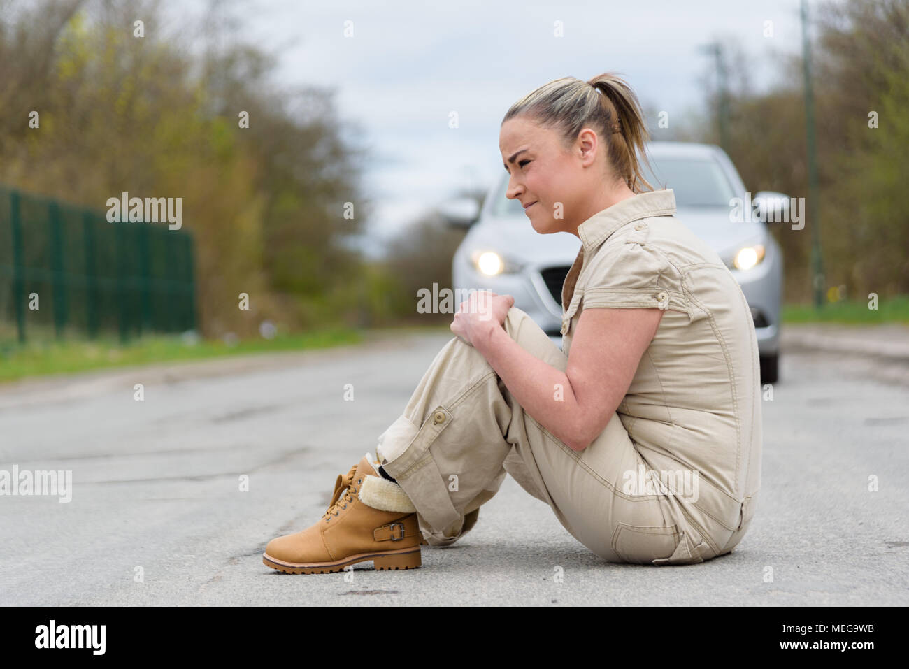 An injured young woman experiencing severe pain caused by knee sprain or fracture after car accident. Stock Photo