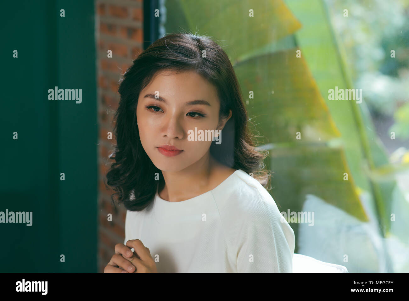 Asian sad woman thinking while sitting on bed at home near big window. Stock Photo