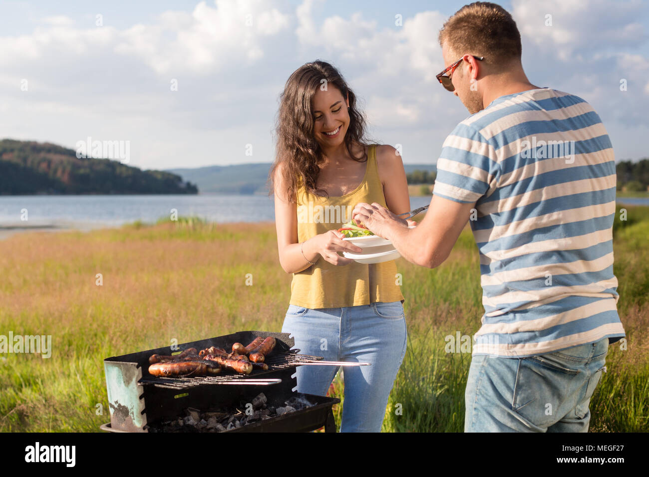 Man and woman having barbecue at lakeside in nature Stock Photo