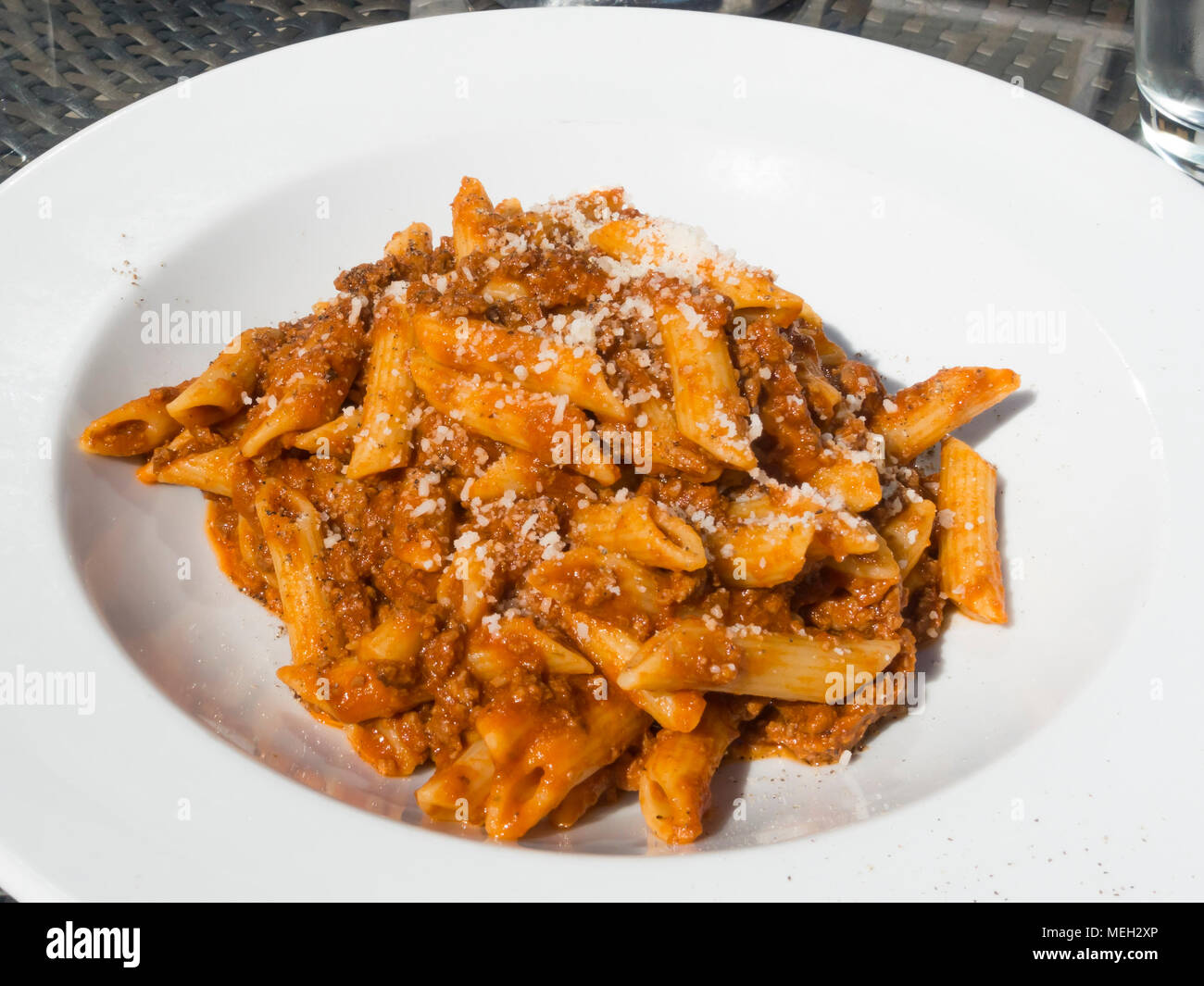 Italian Restaurant Main Course Penne Pasta Bolognese with grated Parmesan cheese and black pepper on a white plate Stock Photo