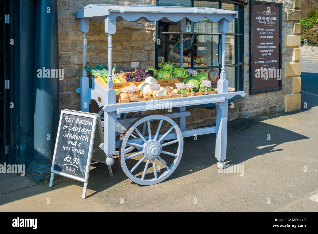 A market stall made like an old fashioned hand barrow with fresh vegetables for sale outside a café in Helmsley Market Place North Yorkshire Stock Photo