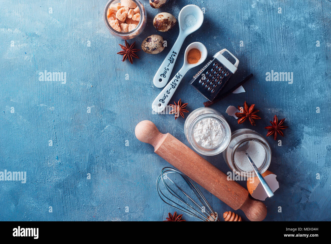 Flat lay pastry preparation concept. Baking ingredients flat lay with flour, sugar, cinnamon, anise, eggs, rolling pin, grinder, honey spoons and measuring spoons. Concrete background with copy space Stock Photo