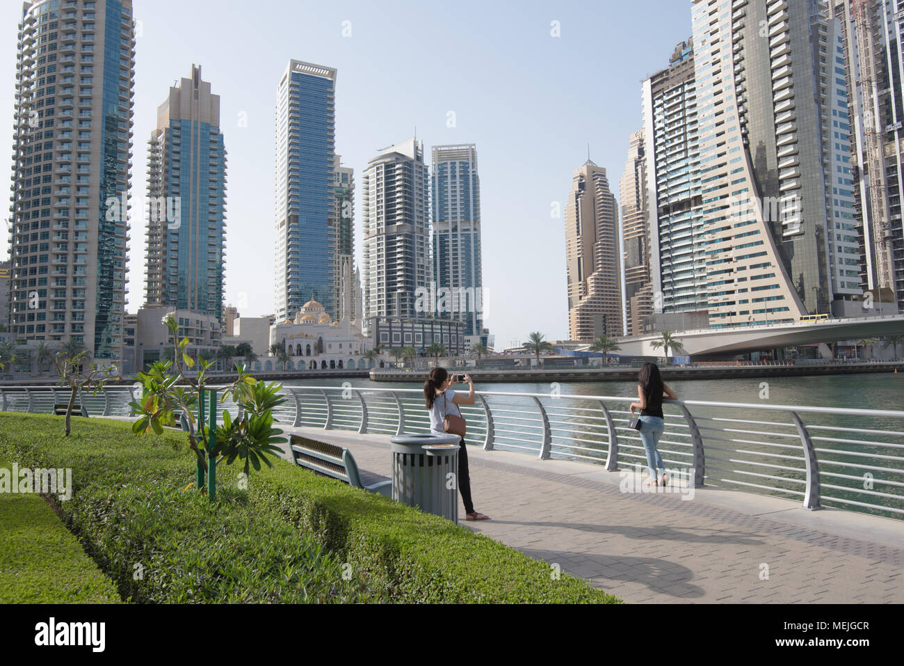 Walkers pause to take photos against the backdrop of tall skyscrapers  surrounding Dubai marina Stock Photo - Alamy