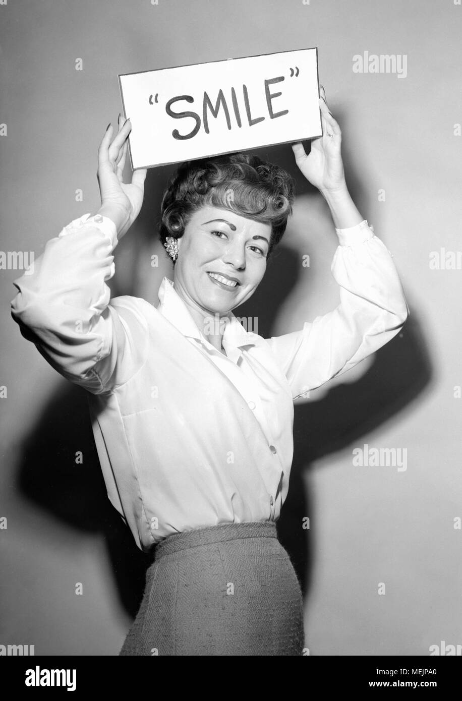 A well-made up 50s woman implores her audience to smile, ca. 1957. Stock Photo