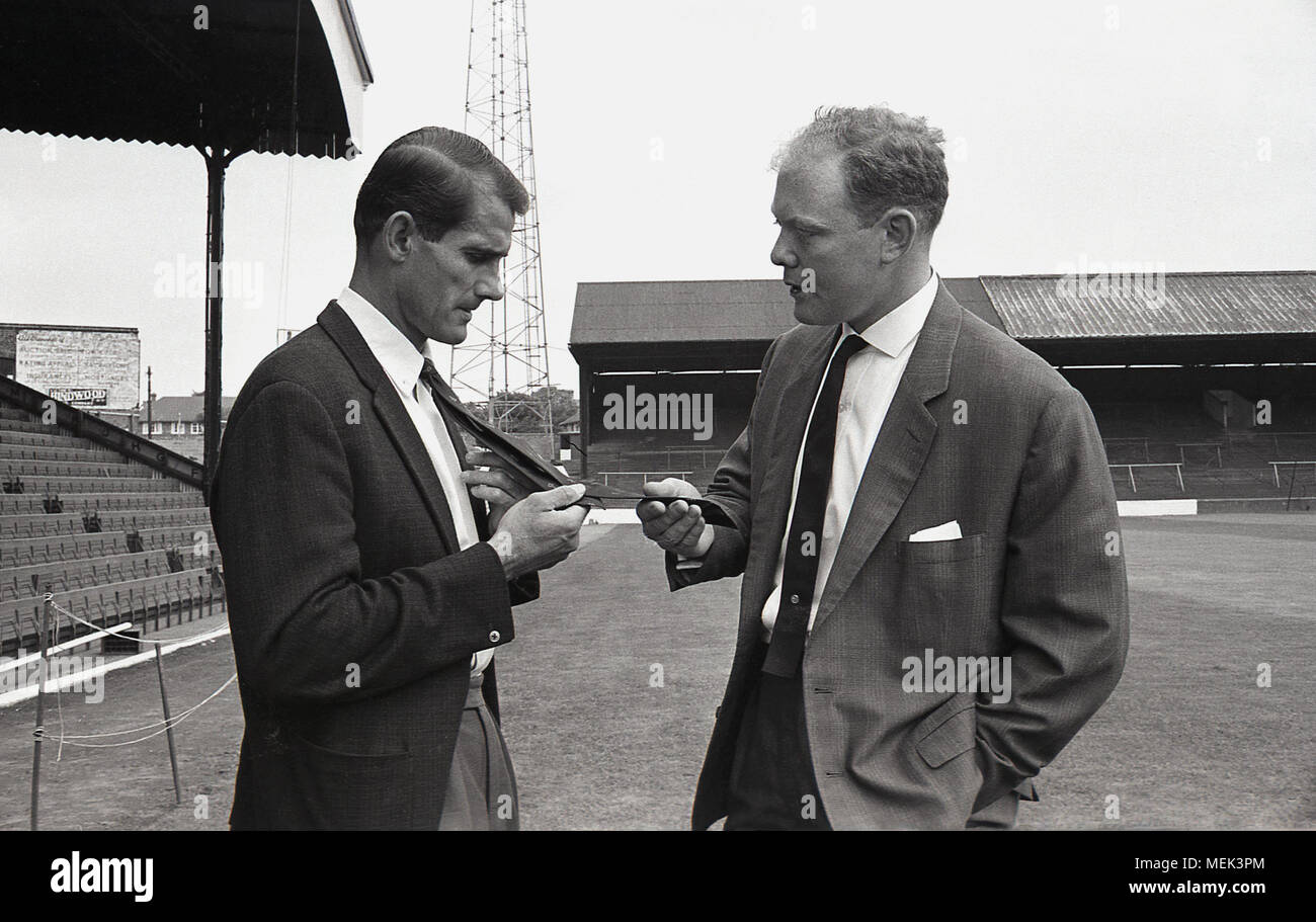 1964, Charlton Athletic FC, historical picture, on the pitch at The Valley, a Charlton footballer shows a local newspaper reporter his new football club official tie. Between 1964 and 1966 the Charlton players wore a new kit, an all white kit with red shoulders. The hand and sword badge first appeared on the football shirt and on the club tie. Stock Photo