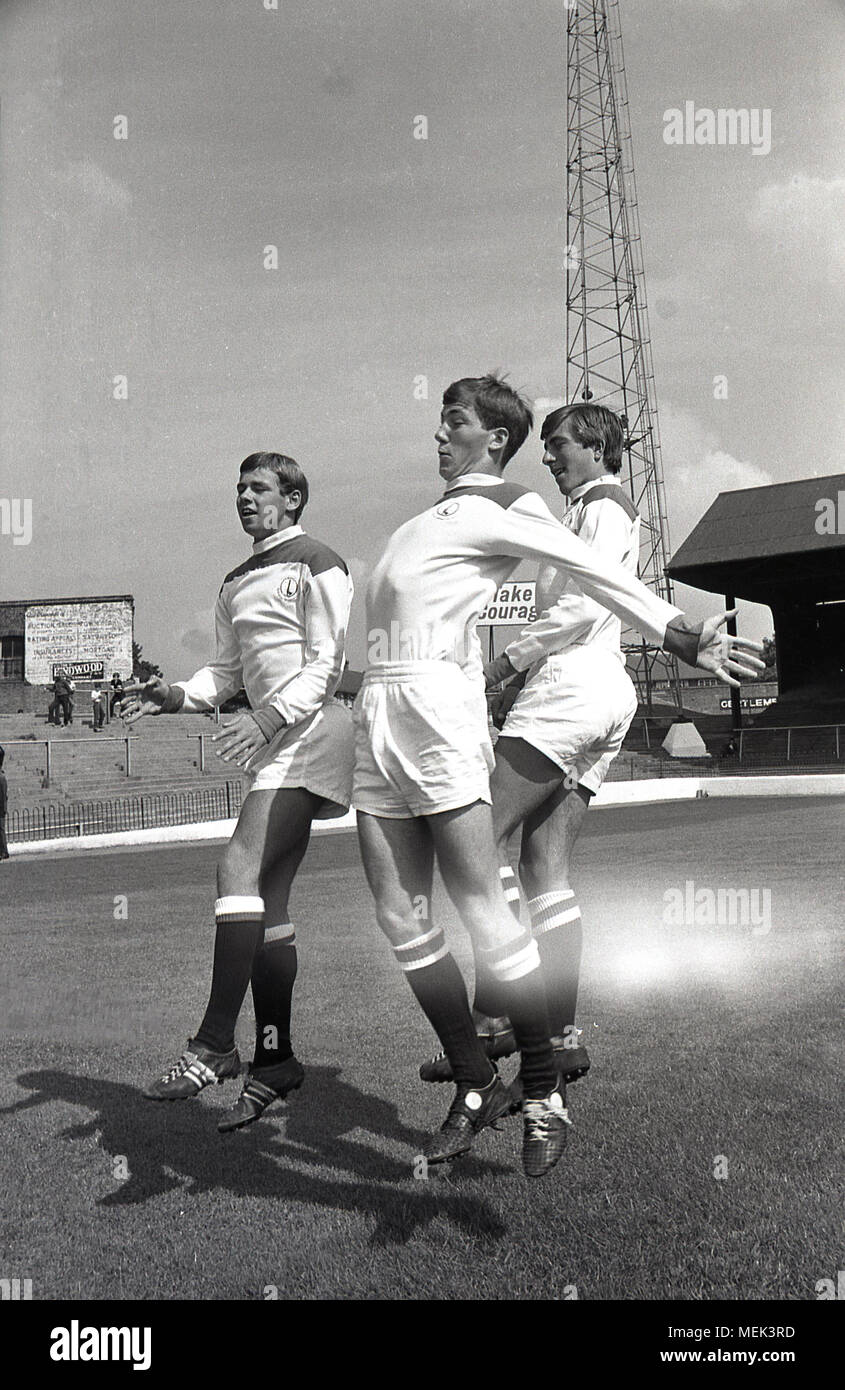 1964, Charlton Athletic FC, historical picture showing three Charlton football players including Billy Bonds on the pitch at the Valley, their  ground, leaping up showing off their new football kit. Between 1964 and 1966 the Charlton players wore a smart all white kit with red shoulders and the hand and sowrd badge first appeared on the shirt. Stock Photo