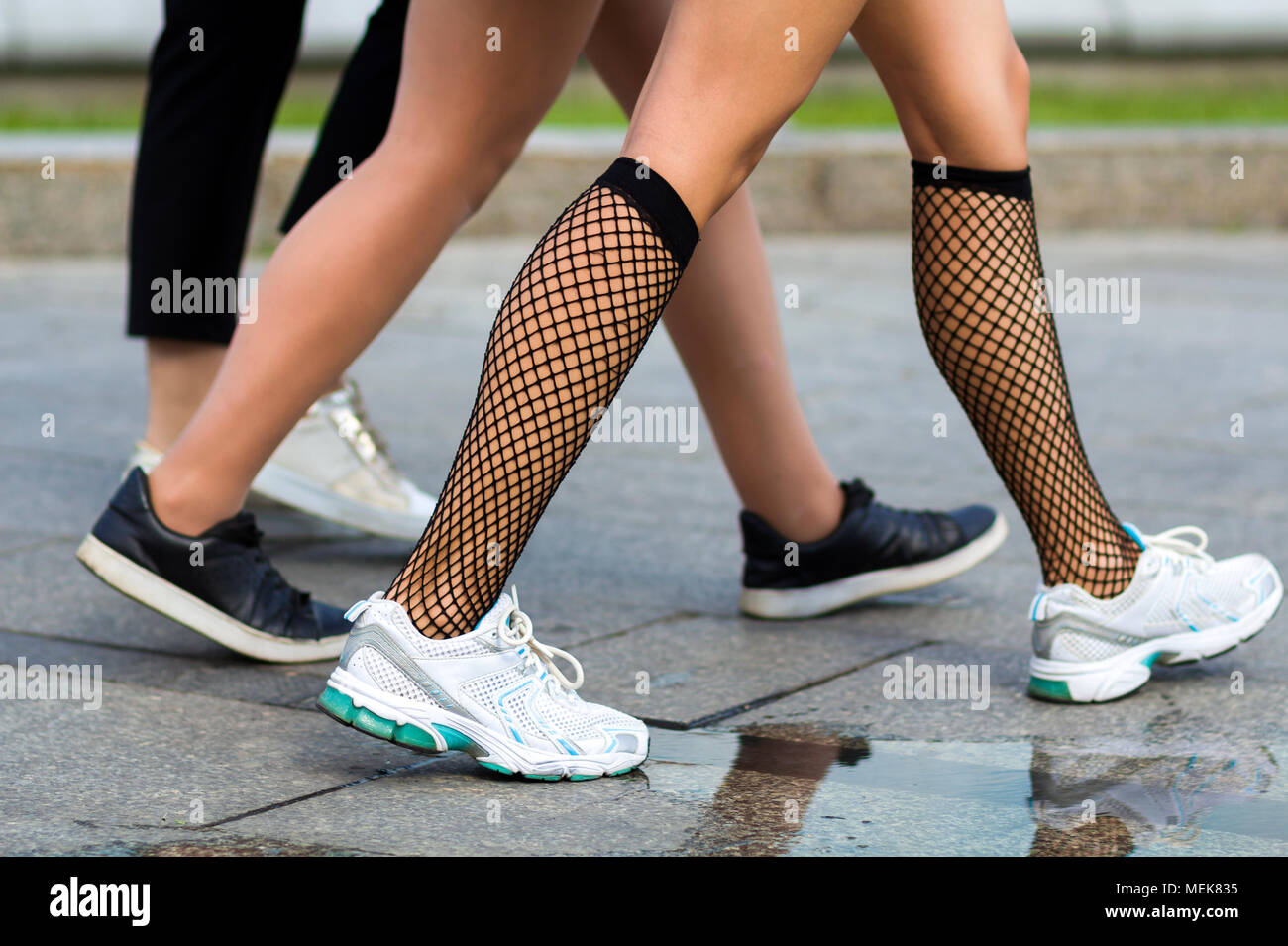 Three pairs of slim fit young girls legs in different sport shoes walking  fast along the concrete road.Busy city lifestyle Stock Photo - Alamy