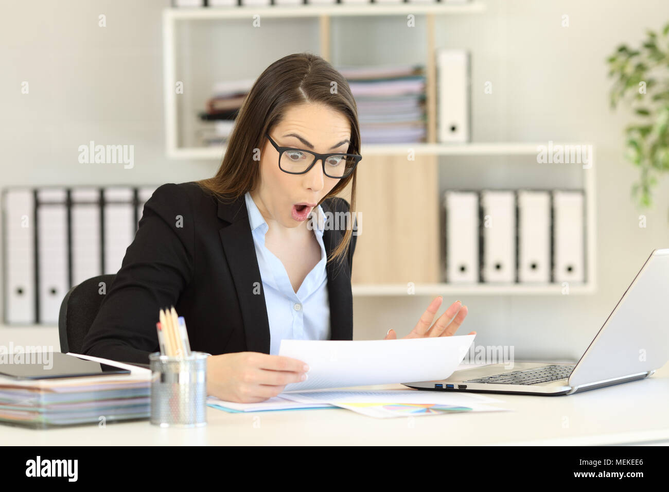 Amazed office worker reading sales report sitting in a desktop at workplace Stock Photo