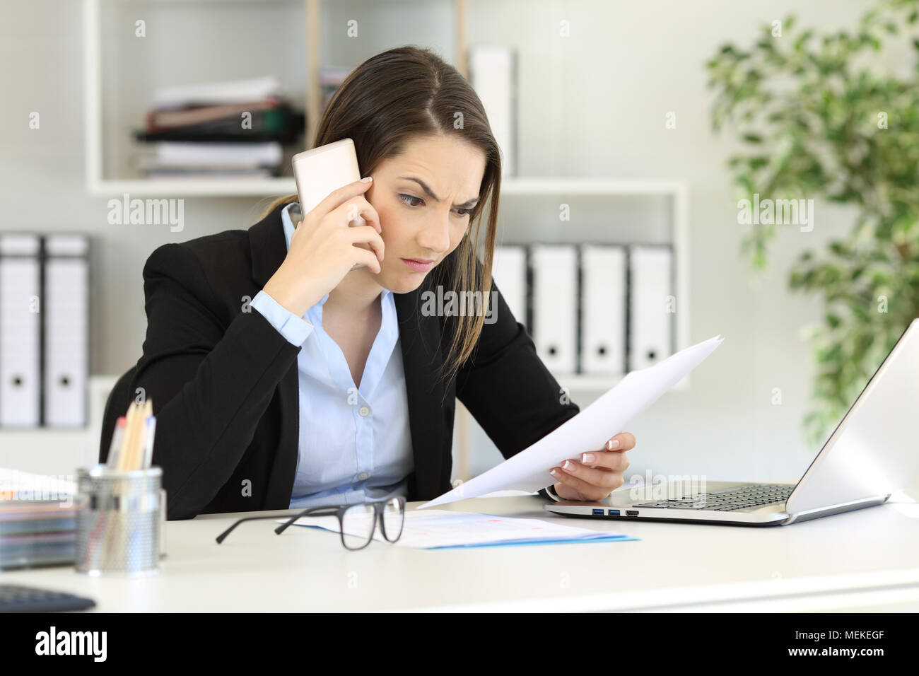 Angry executive calling on phone reading a paper document at office Stock Photo