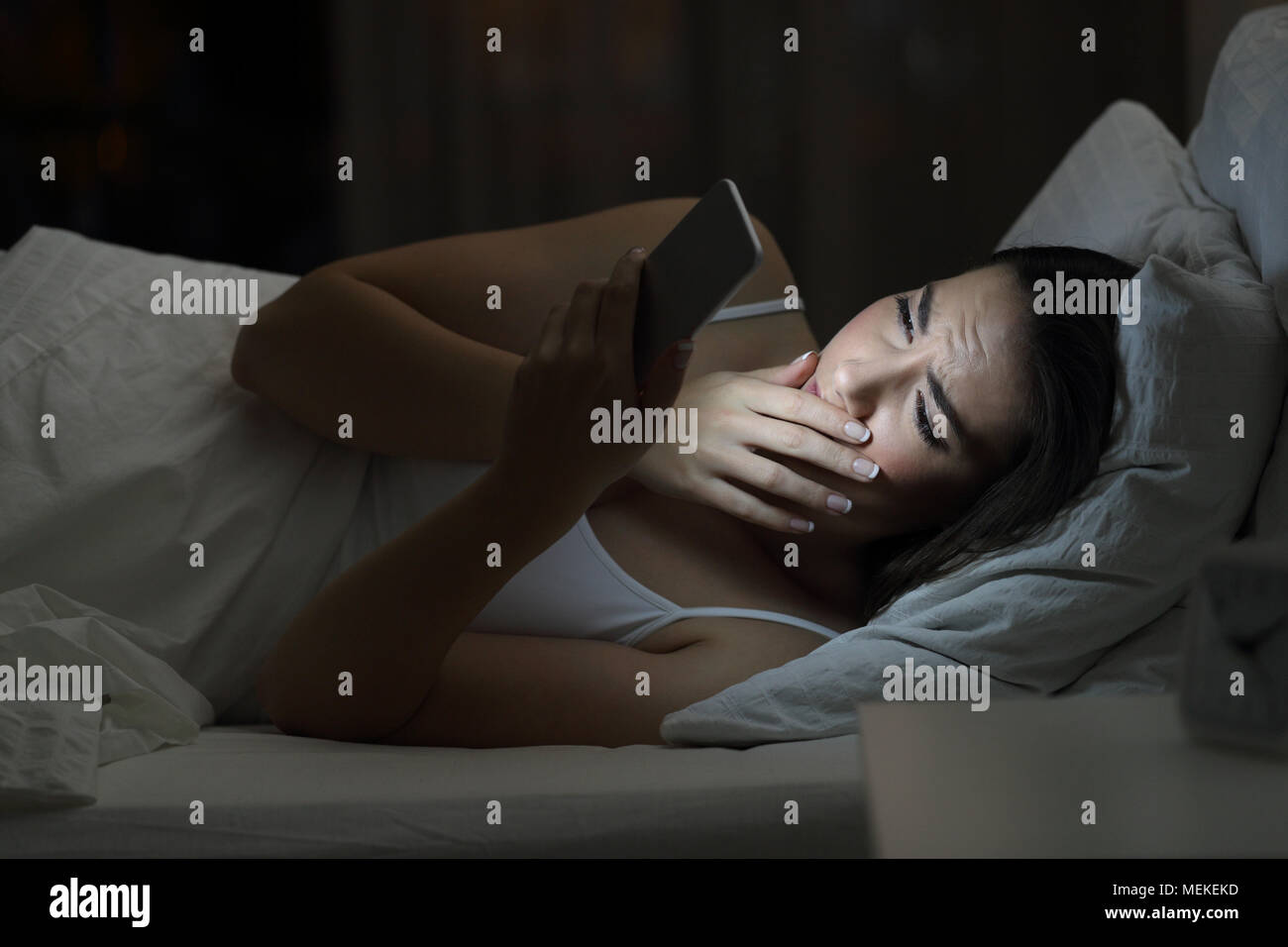 Concerned woman finding bad news in a smart phone on line in the night on the bed at home with a dark background Stock Photo