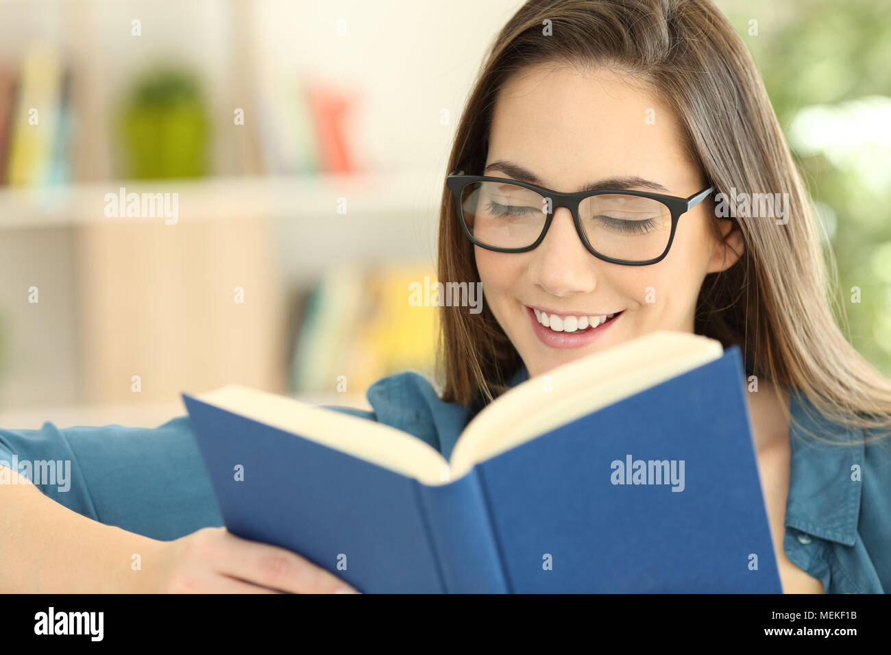 Happy girl wearing eyeglasses reading a paper book sitting on a couch