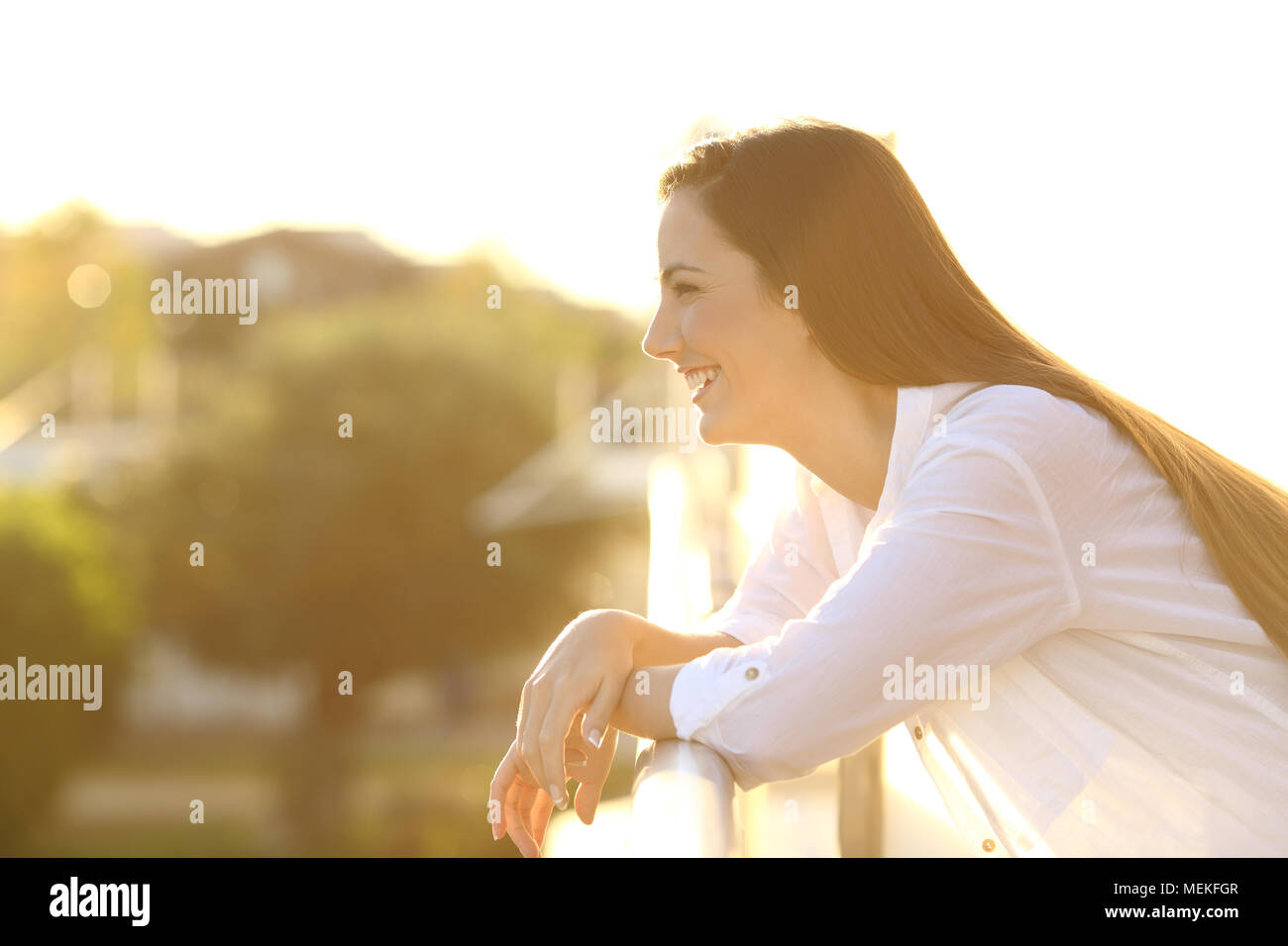 Side view portrait of a happy brunette woman looking away in a balcony at sunset Stock Photo