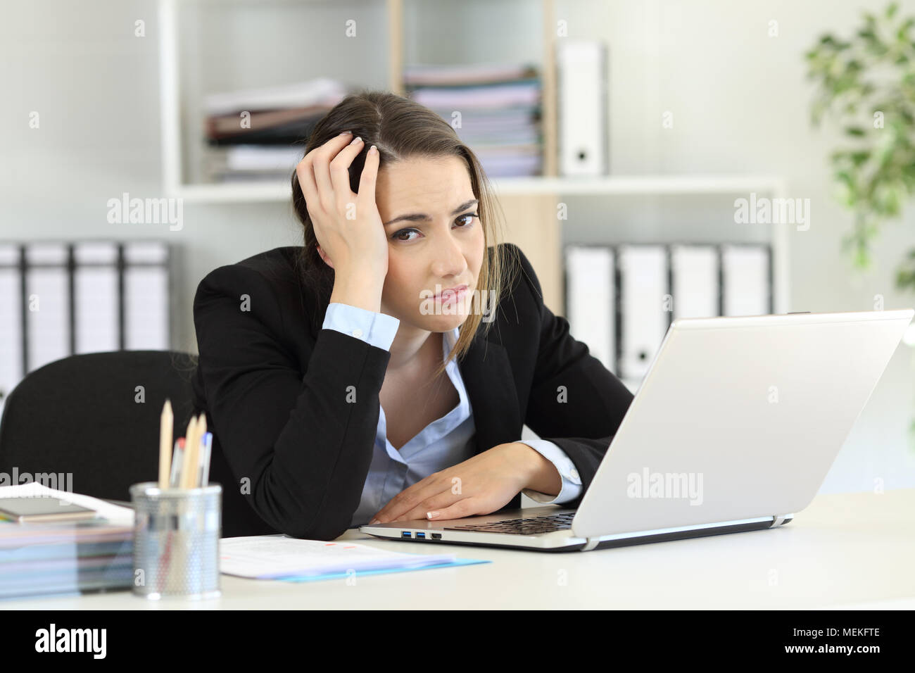 Worried office worker looking at camera sitting in a desk at workplace Stock Photo